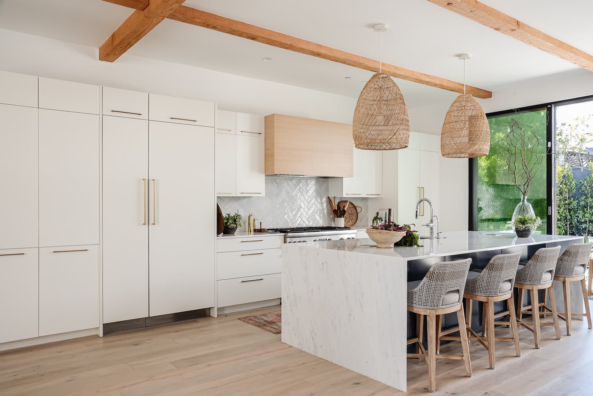 Bright, organized kitchen with a marble waterfall island, woven counter stools and rattan pendants