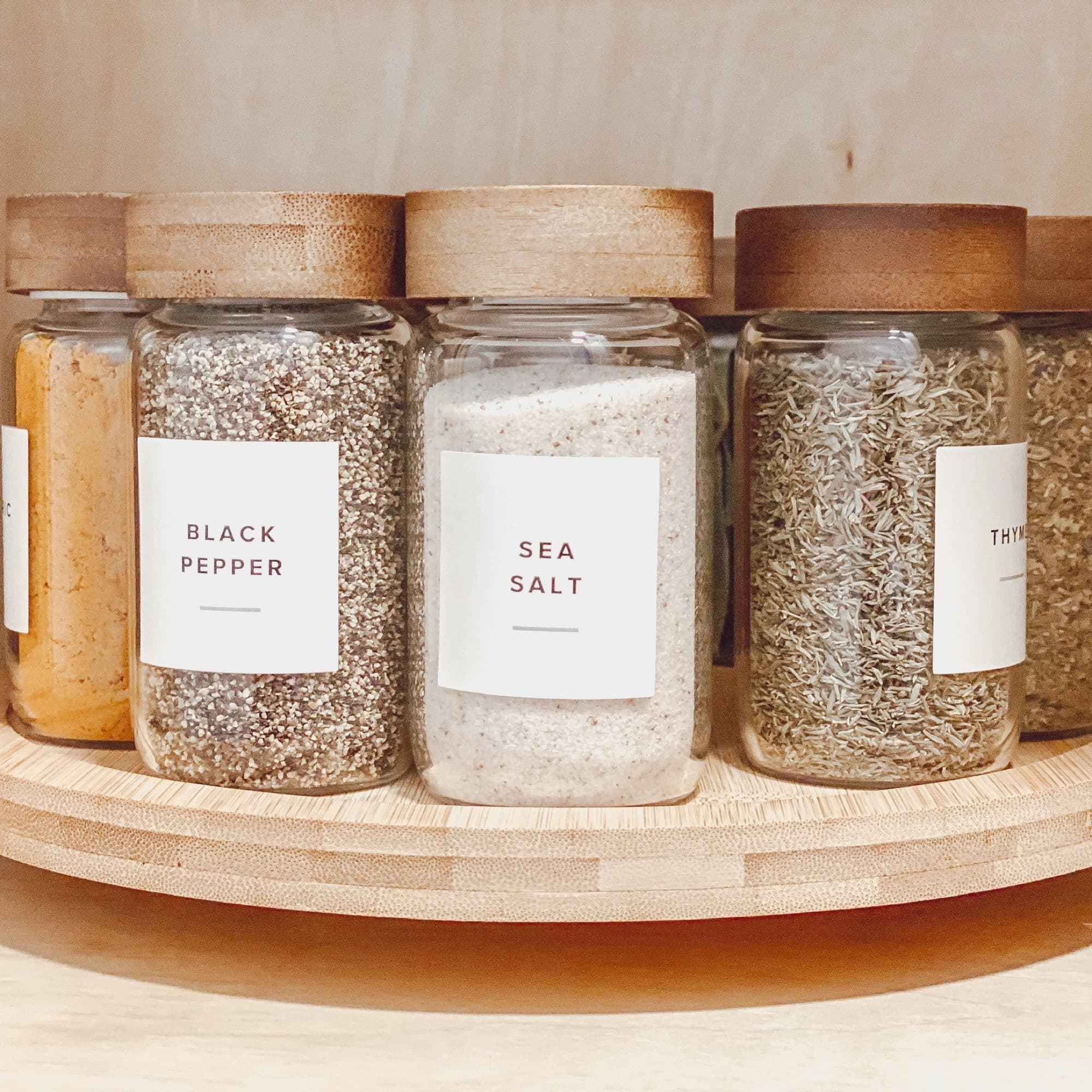 Labeled glass spice jars with bamboo lids on a wood turntable