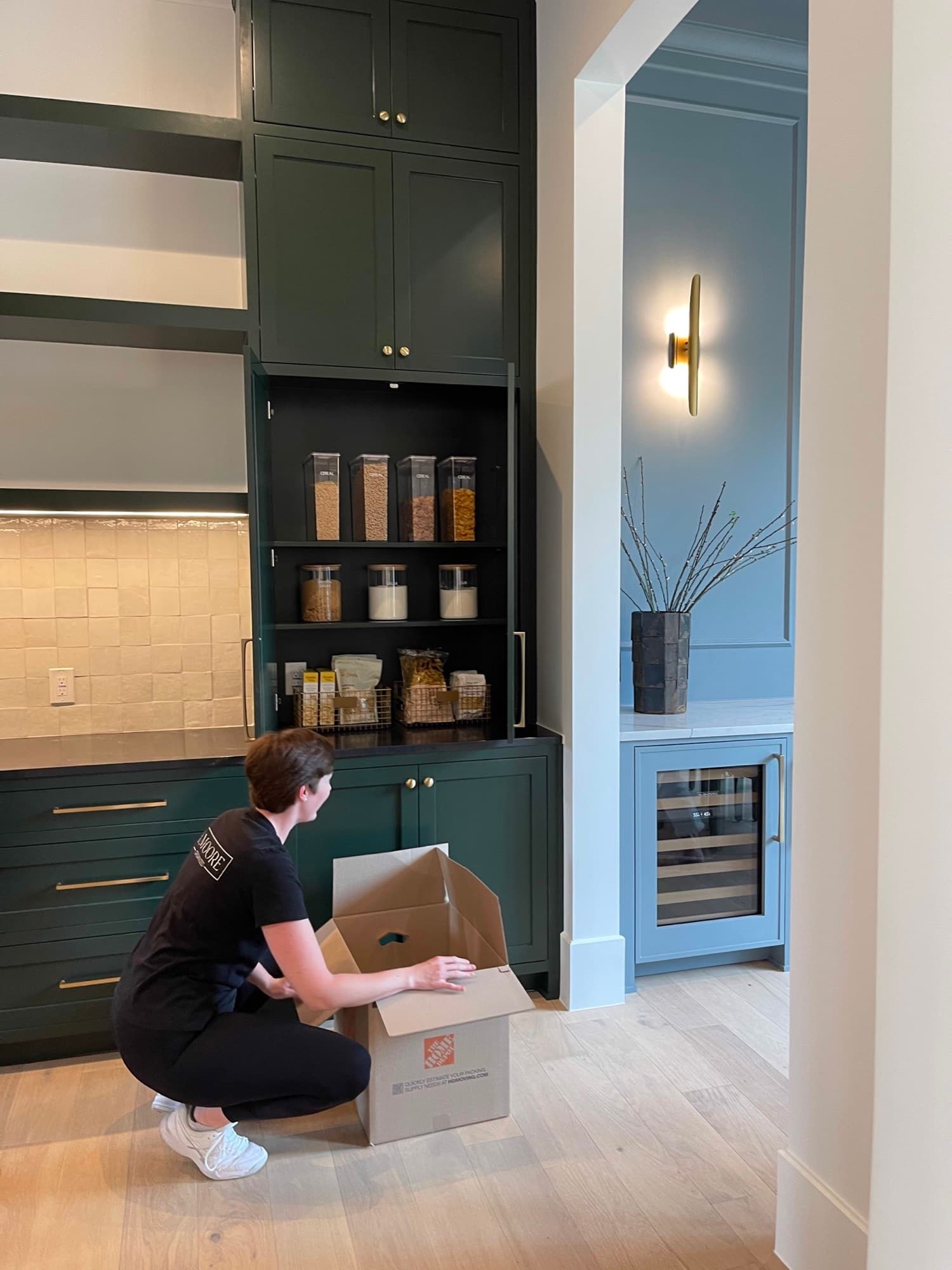 Organizer unpacking a moving box at a dark green butler's pantry