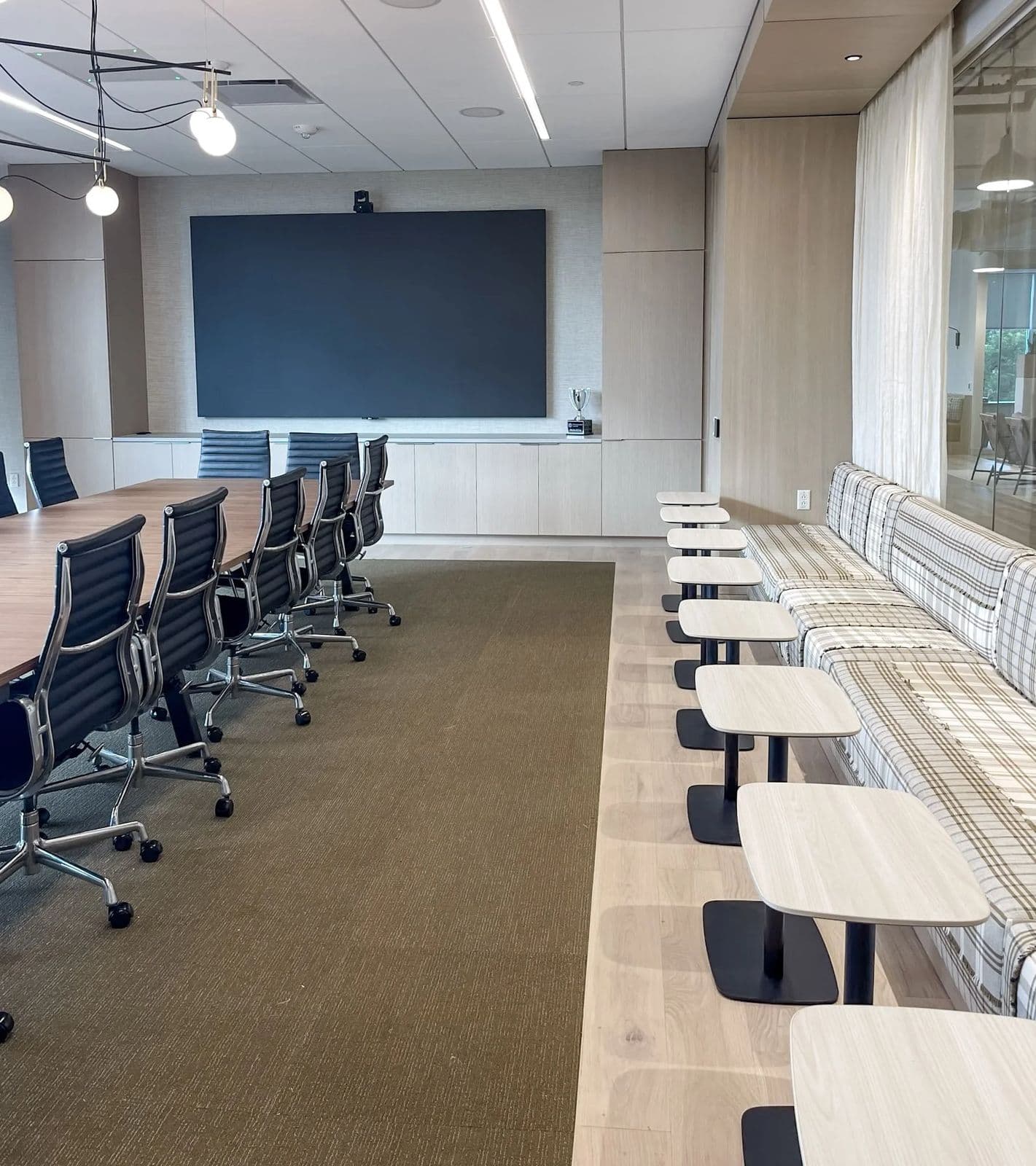 Organized conference room with a long table, black chairs and a wall screen