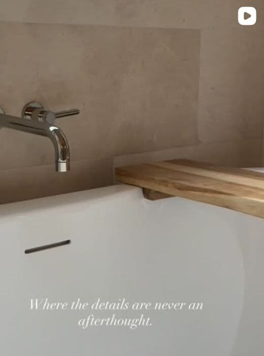 Wall-mounted faucet over a stone tub with a wood tray, captioned: Where the details are never an afterthought.