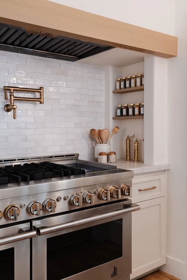 White kitchen range with a brass pot filler and open spice shelves