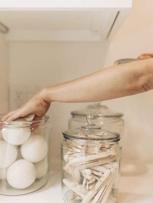 Glass jars of wool dryer balls and clothespins in a laundry cabinet