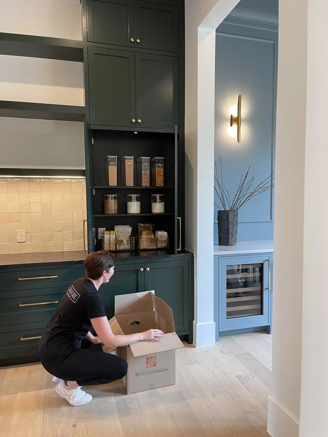 A B. Moore organizer unpacking a moving box beside a dark green pantry