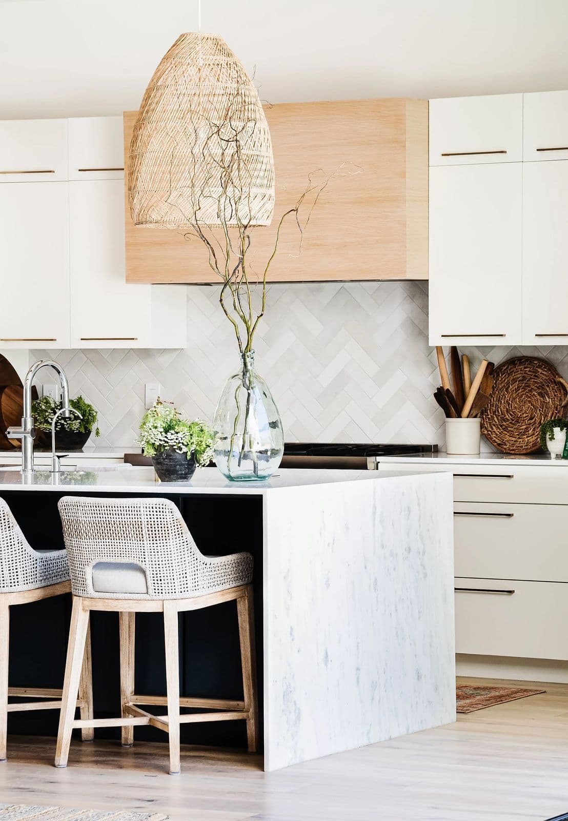 Bright kitchen with a marble waterfall island, woven counter stools and a glass vase of branches