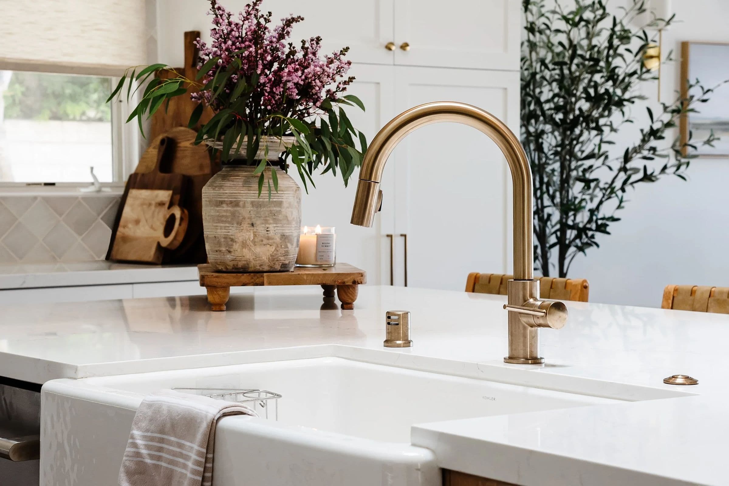 Farmhouse sink with a brass faucet, fresh flowers and wood boards