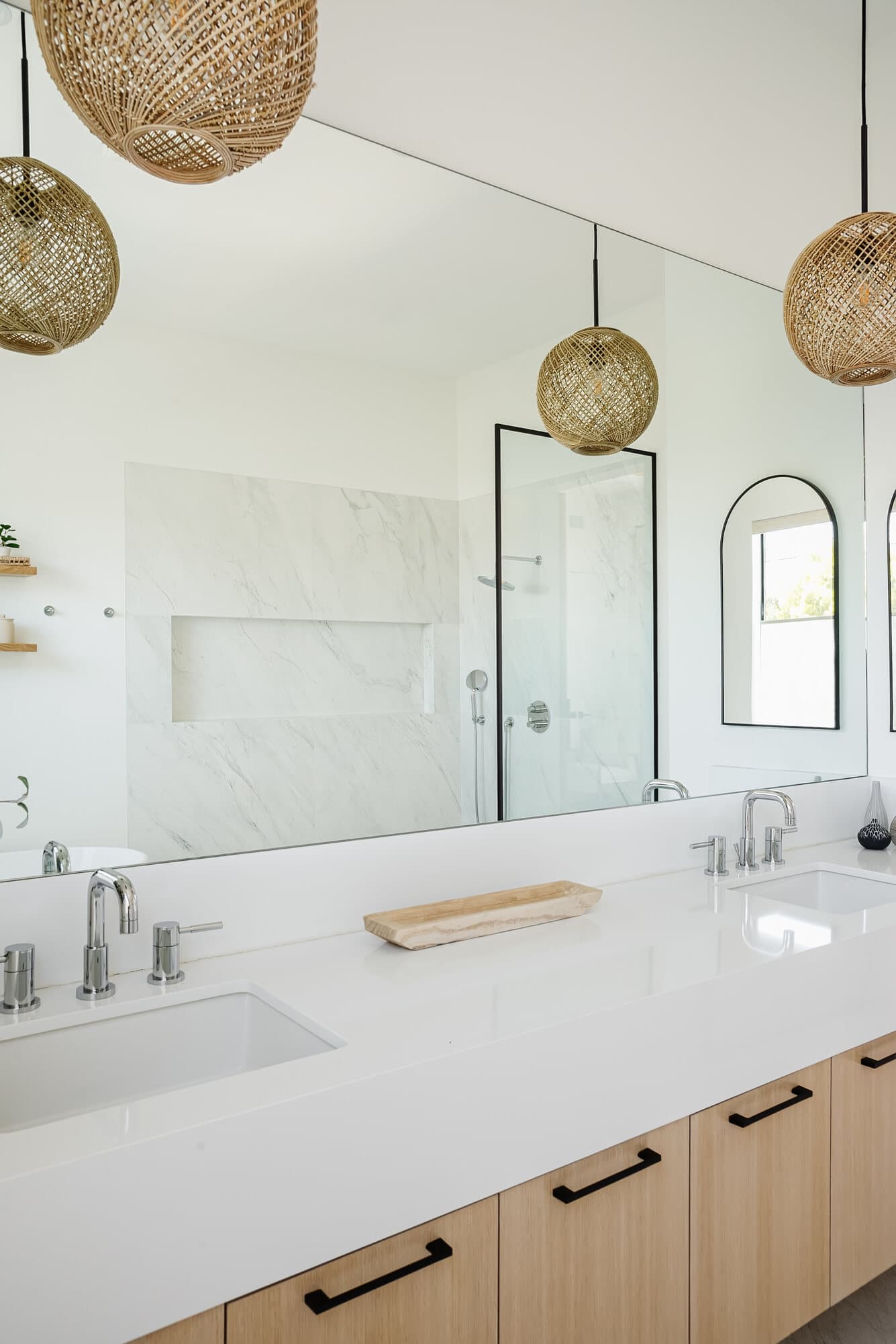 Bright white bathroom with a marble double vanity, black hardware, and an arched mirror