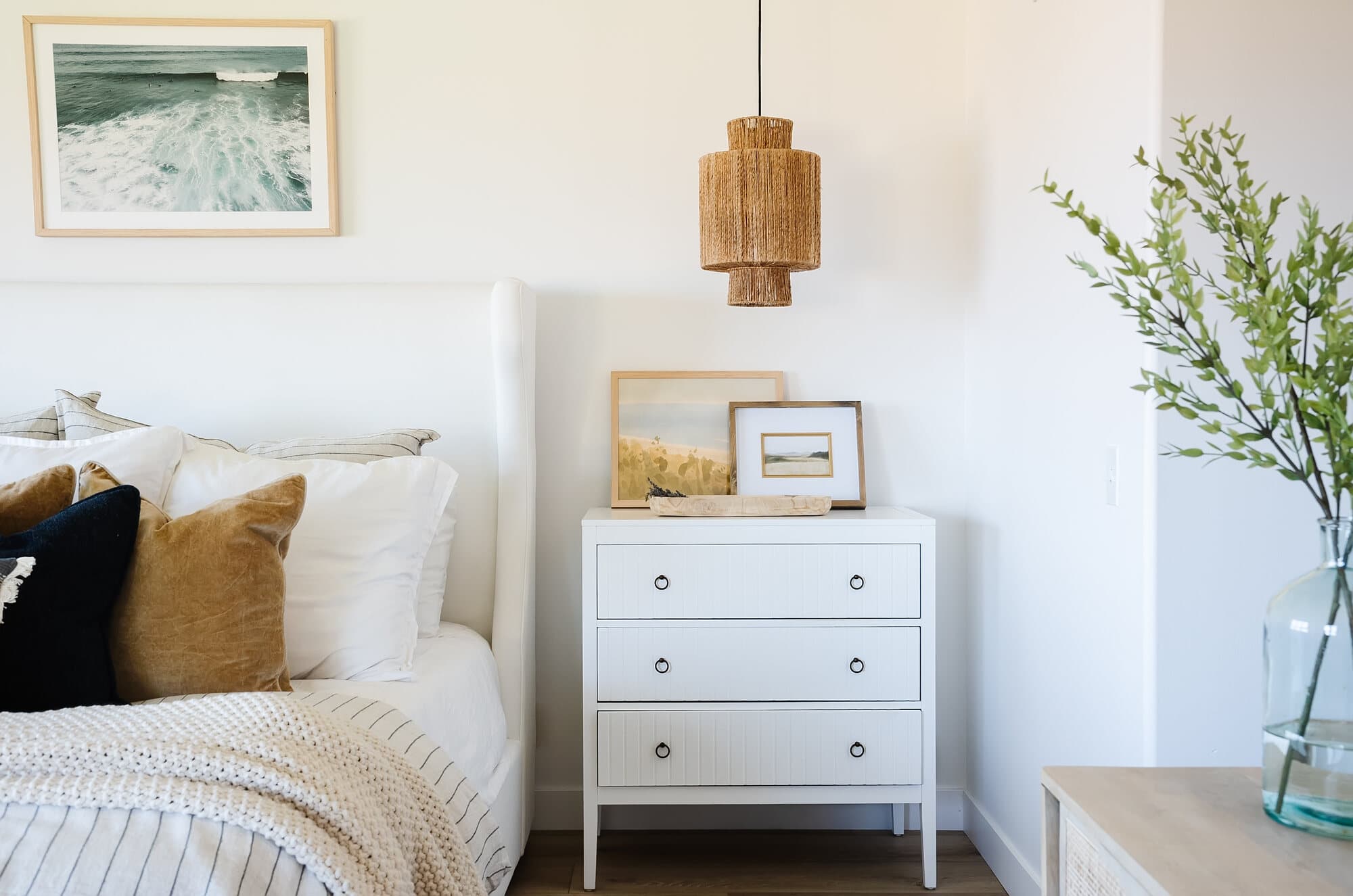 Airy bedroom with a white dresser, framed artwork, and fresh greenery