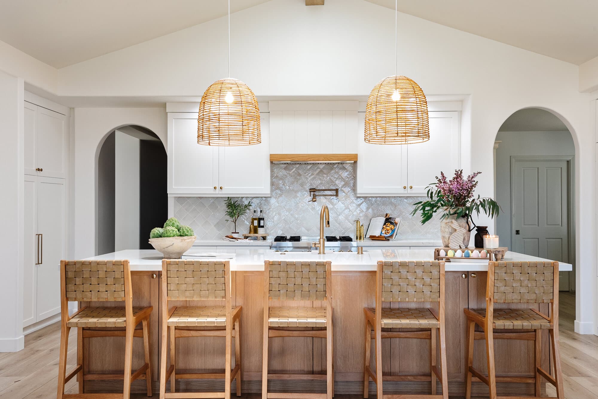Bright white kitchen with arched doorways, rattan pendants, and a marble island