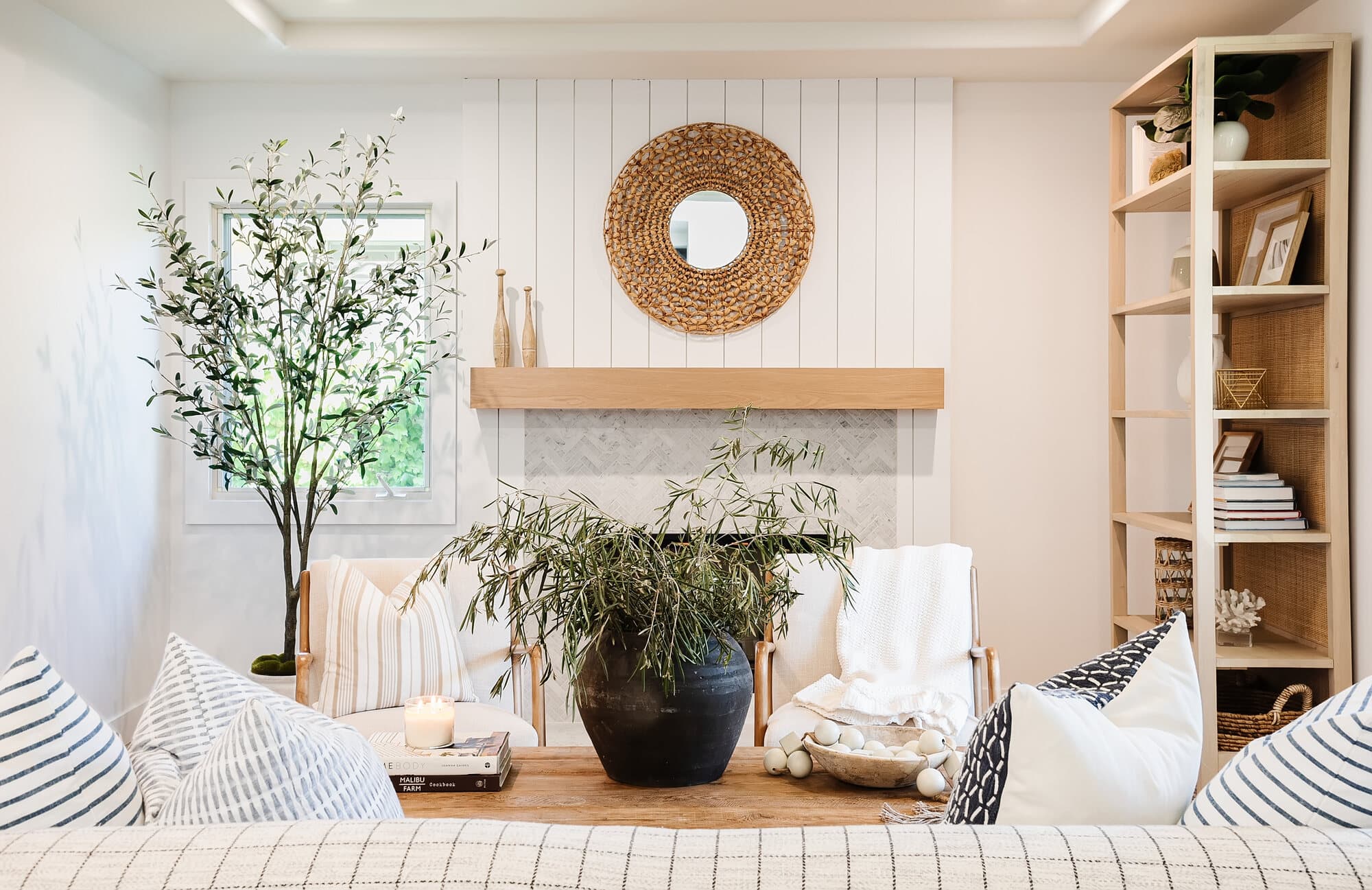 Living room with a shiplap fireplace, styled open shelves, and an olive tree