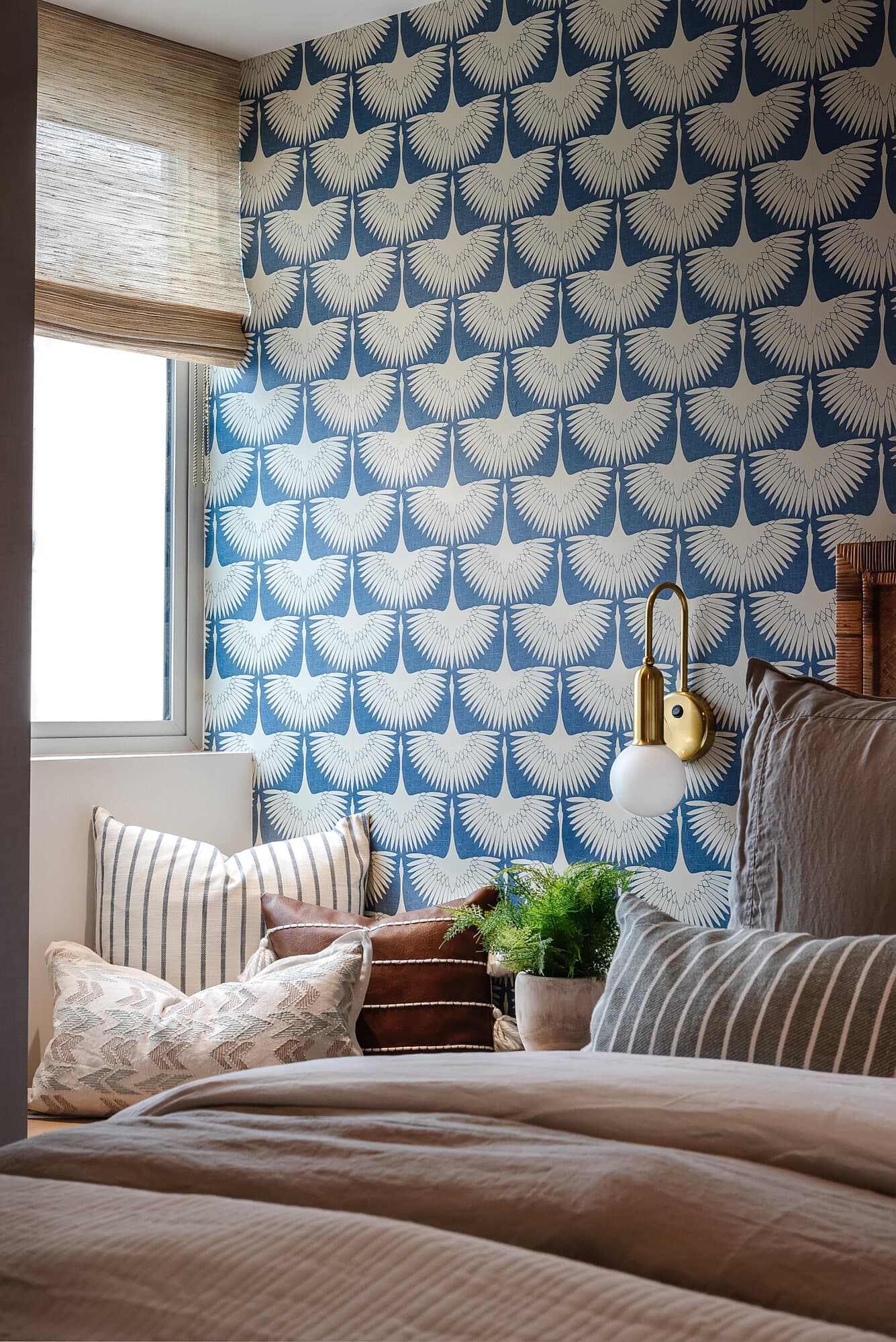 Bedroom with a blue-and-white botanical wallpaper accent wall, brass sconce, and layered bedding
